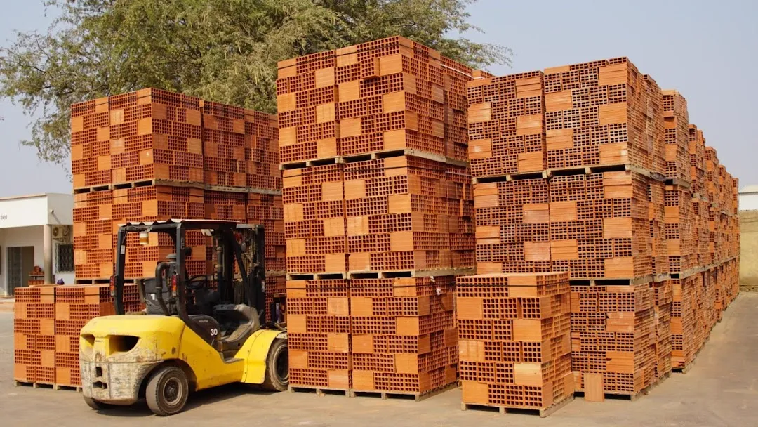 Paletes de tijolos cerâmicos empilhados no pátio da fábrica, com um empilhador amarelo à frente